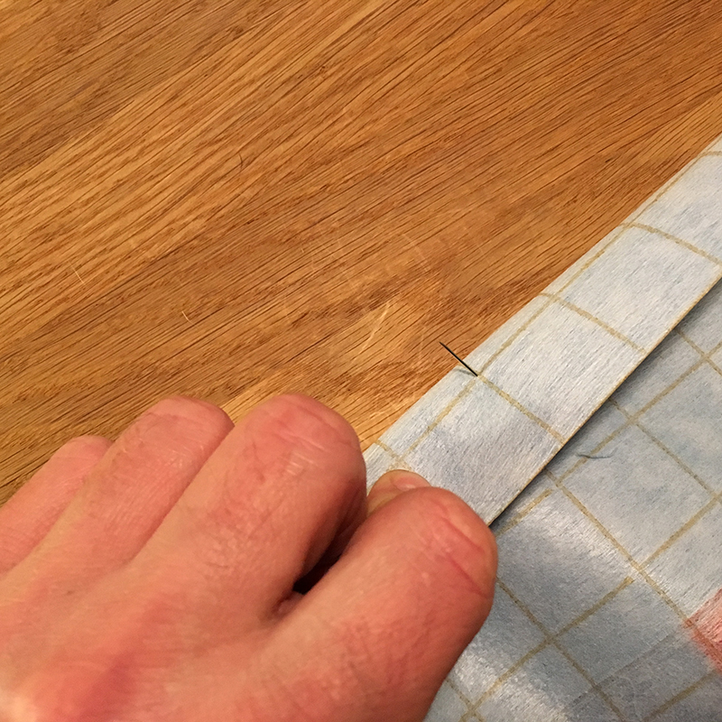 The pin comes out on the intersection of the grid-lines on the back of the folded fabrlc, meaning the seam will be straight and the grid will be aligned.