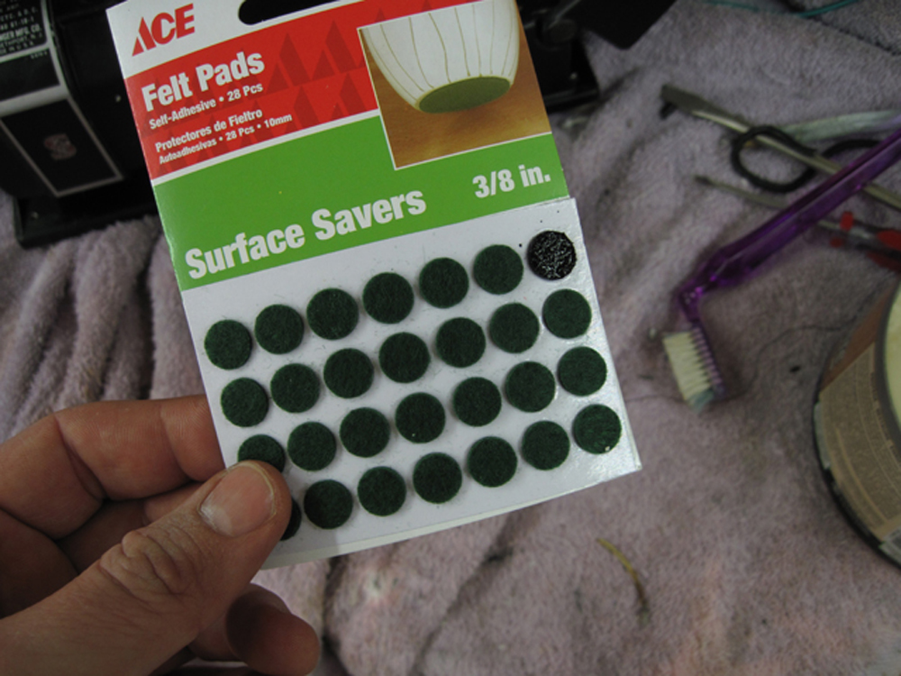 A sheet of felt pads. The package reads, "ACE Felt Pads, Self Adhesive, 24 Pcs. Surface Savers, 3/8 in." One of the pads is dyed black.
